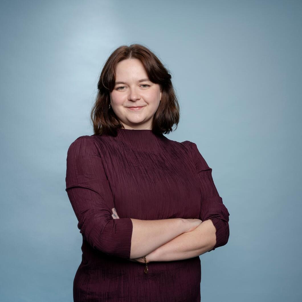 Roos kijkt met haar armen over elkaar glimlachend de camera in