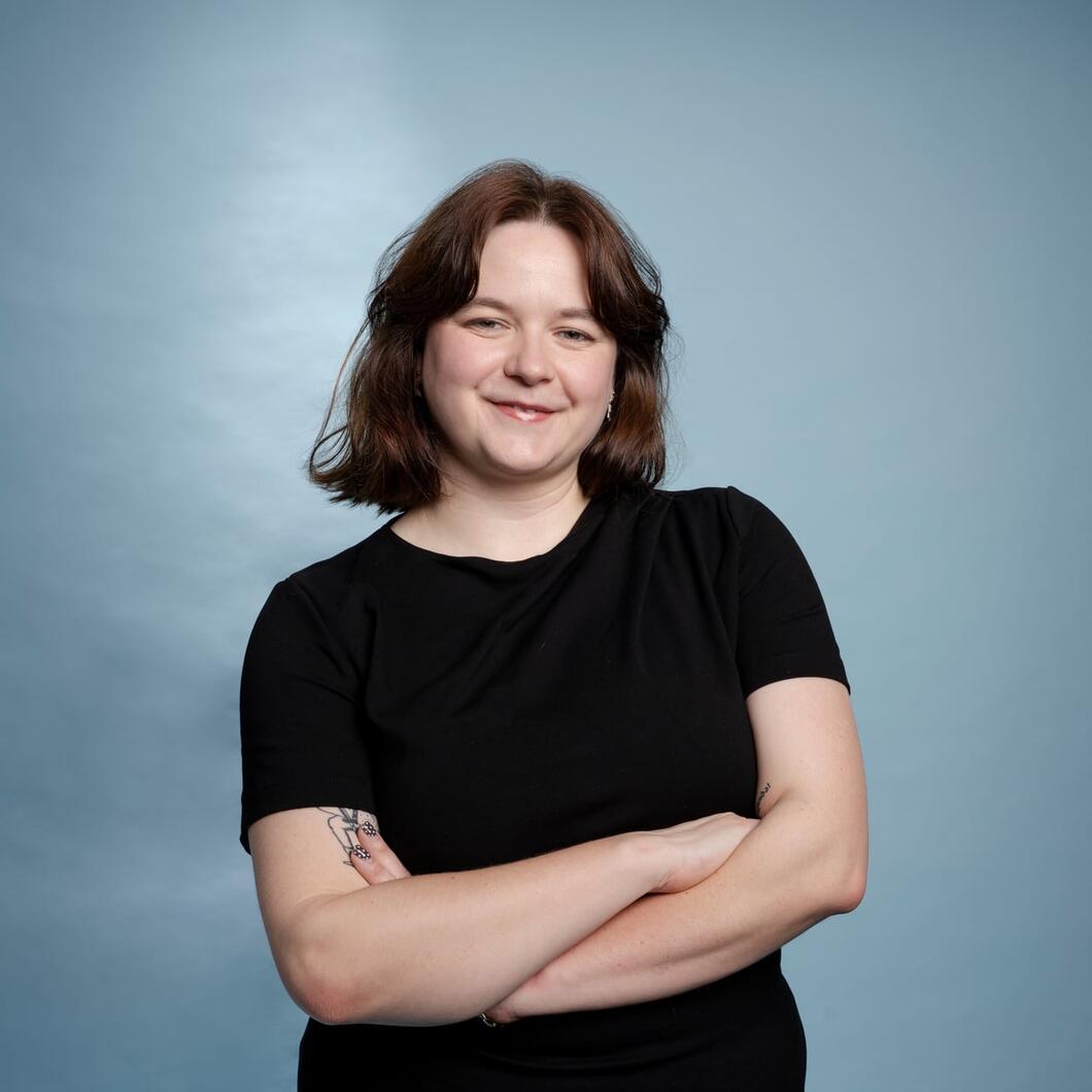 Roos kijkt met haar armen over elkaar glimlachend de camera in