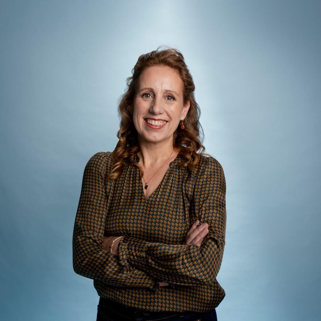 Anneke kijkt met haar armen over elkaar lachend in de camera