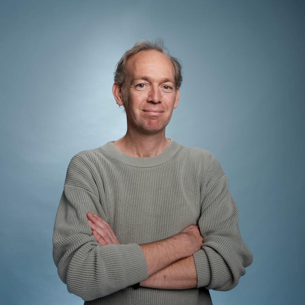 Wijbe kijkt met zijn armen over elkaar glimlachend de camera in