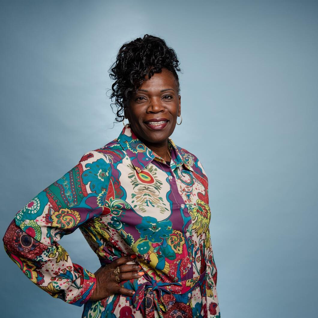 Imelda kijkt met haar hand in haar zij lachend de camera in