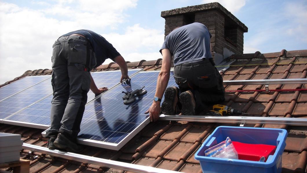 Twee mensen installeren zonnepanelen op het dak van een woning.