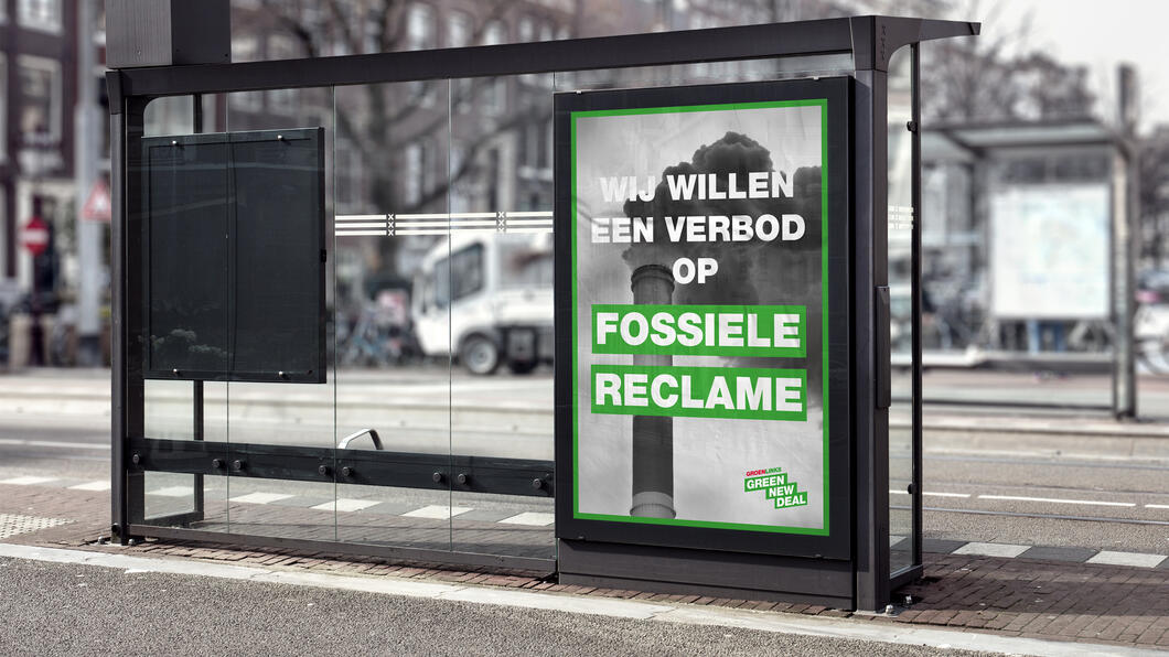 Een foto van een bushokje met een poster van een vieze schoorsteen, met daarom de tekst: "Wij willen een verbod op fossiele reclame"