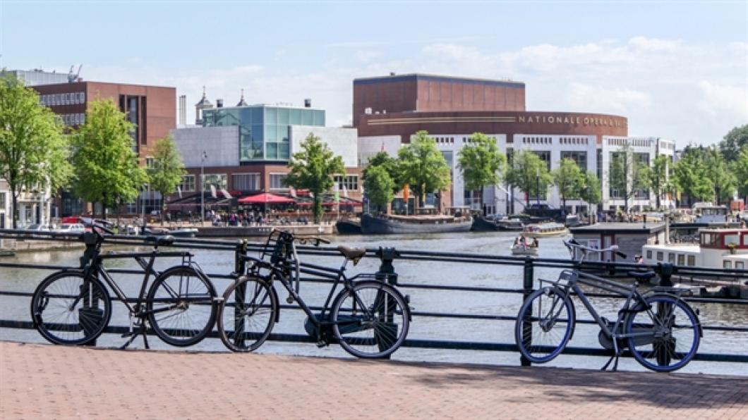 Fietsen op brug over de Amstel met uitzicht op de Stopera/stadhuis