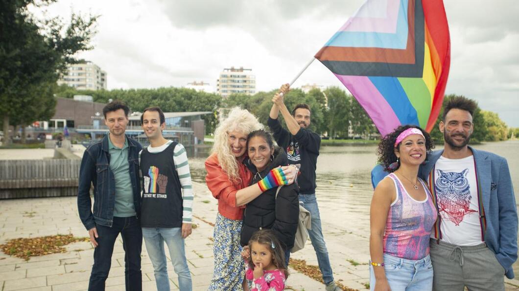 LHBTIQ+ koppels omhelzen elkaar met een regenboogvlag op de achtergrond