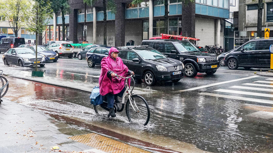 Plassen op de weg met een fietser erin in een roze jas