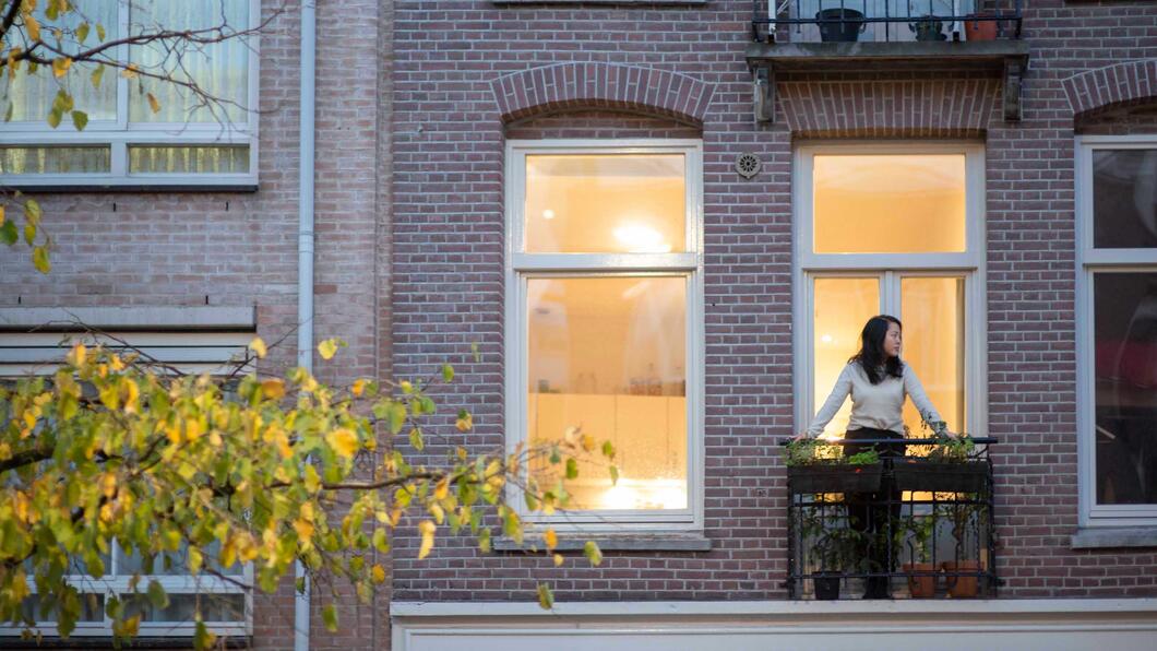 Vrouw staat op balkon van woning op eerste verdieping
