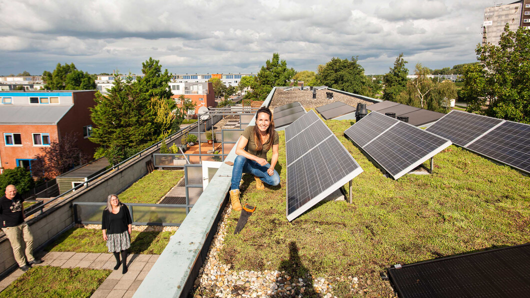 Foto van een lachende vrouw gehurkt op een groen dak met zonnepanelen 