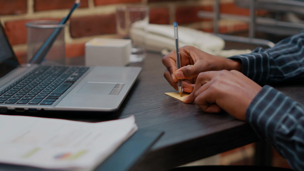 Op een vol bureau schrijft een hand op een post-it