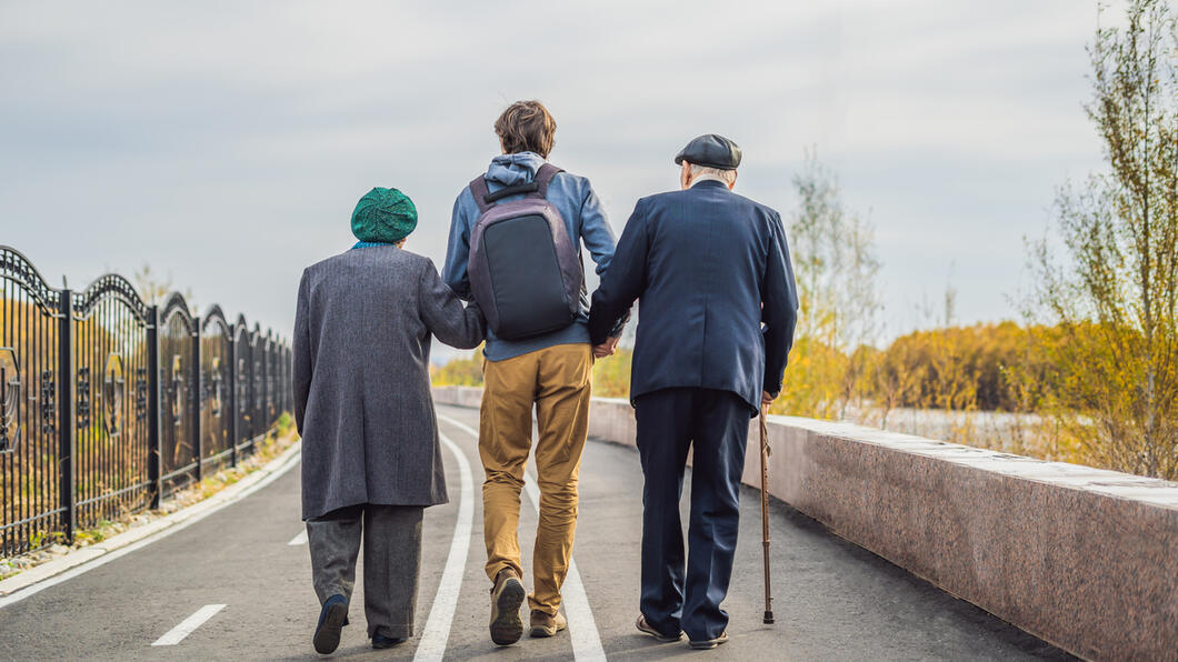 een jonger iemand loopt arm in arm met ouderen