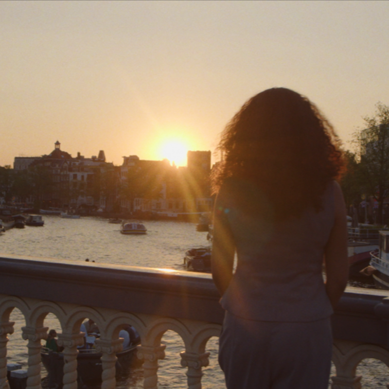 Imane staat op een brug en kijkt naar de zonsondergang