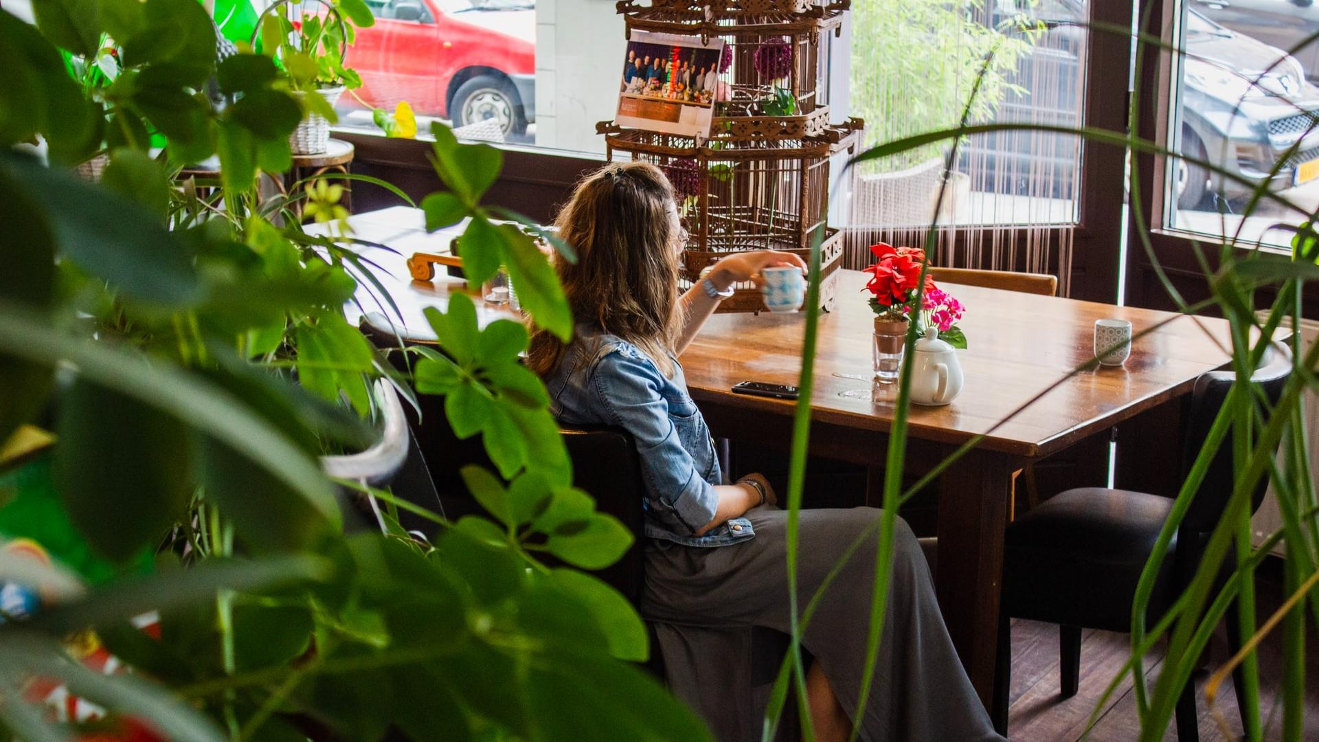 Vrouw zit aan tafel met een kopje thee. Foto: Louis Hansel, Unsplash