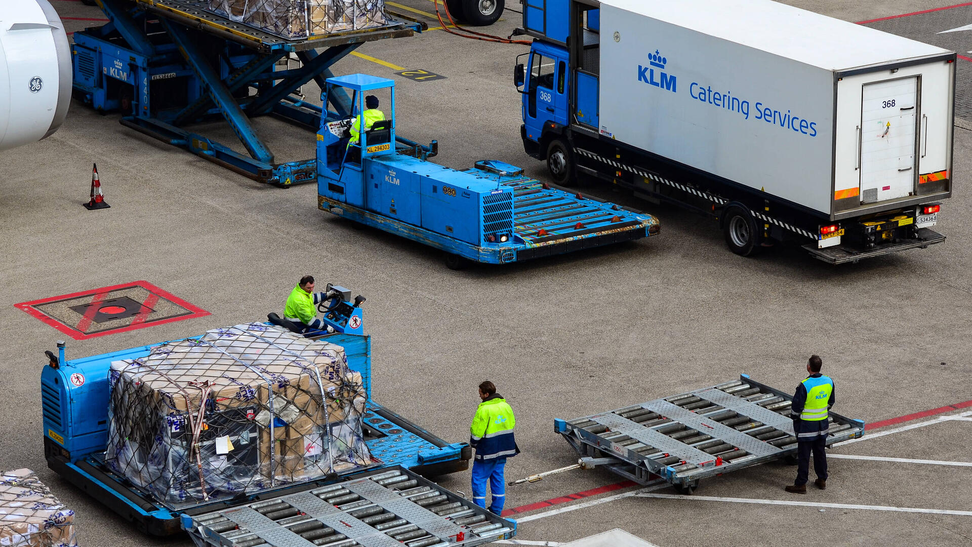 Foto van werknemers op Schiphol die vracht aan vervoeren zijn naar een vliegtuig