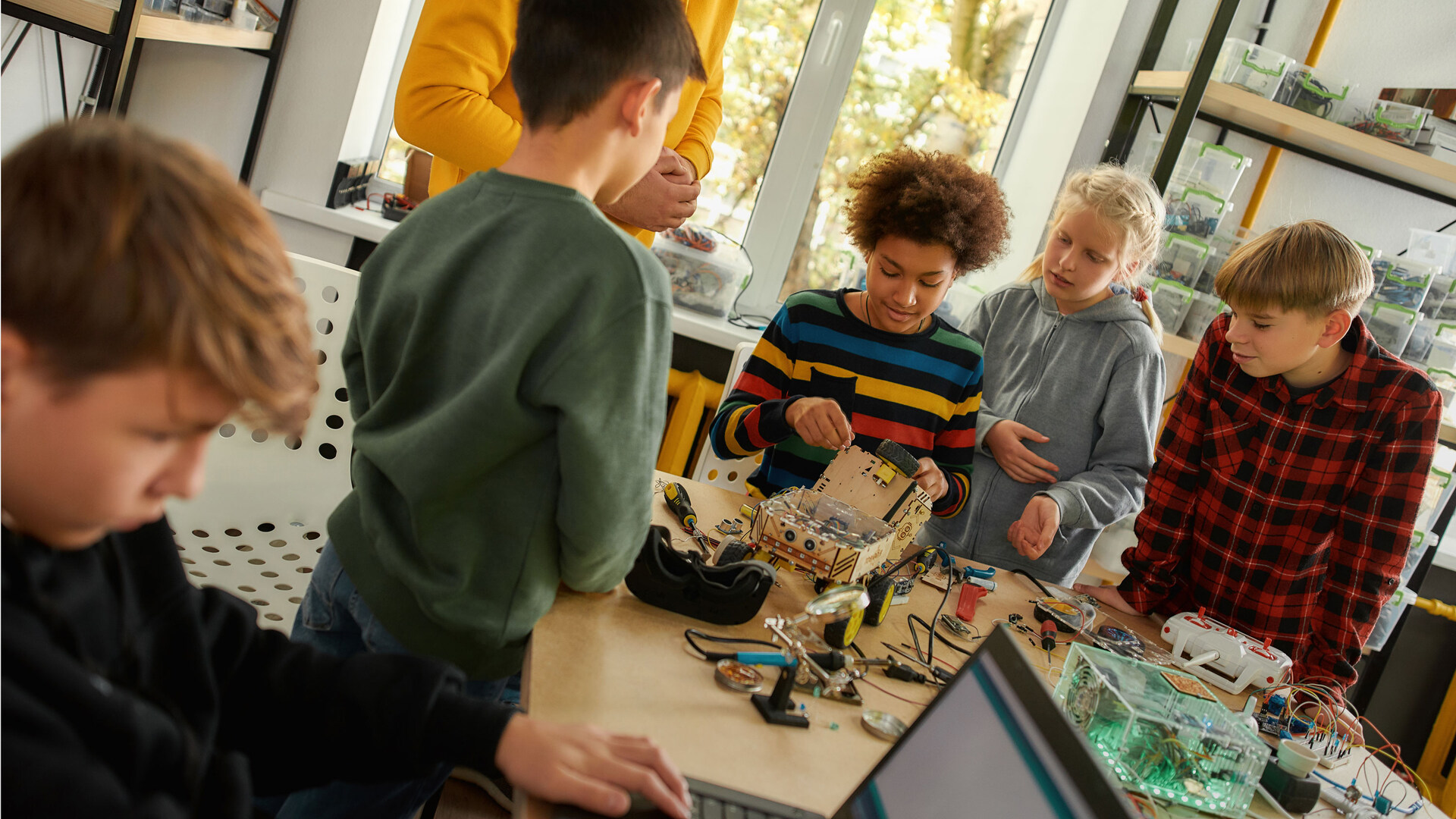 Groep kinderen staat samen met leraar om tafel en werken aan een robotwagentje