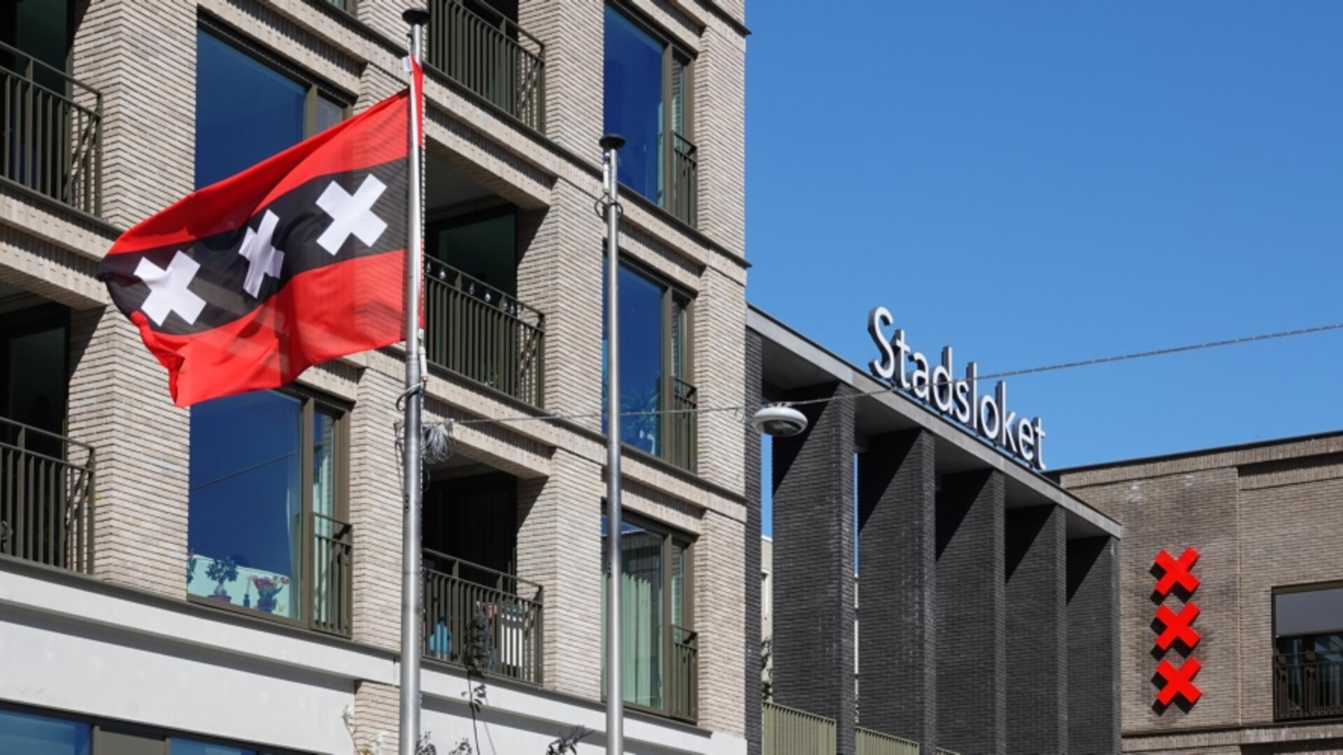 stadsloket in nieuw-west met drie andreaskruizen aan de gevel en een wapperende Amsterdamse vlag