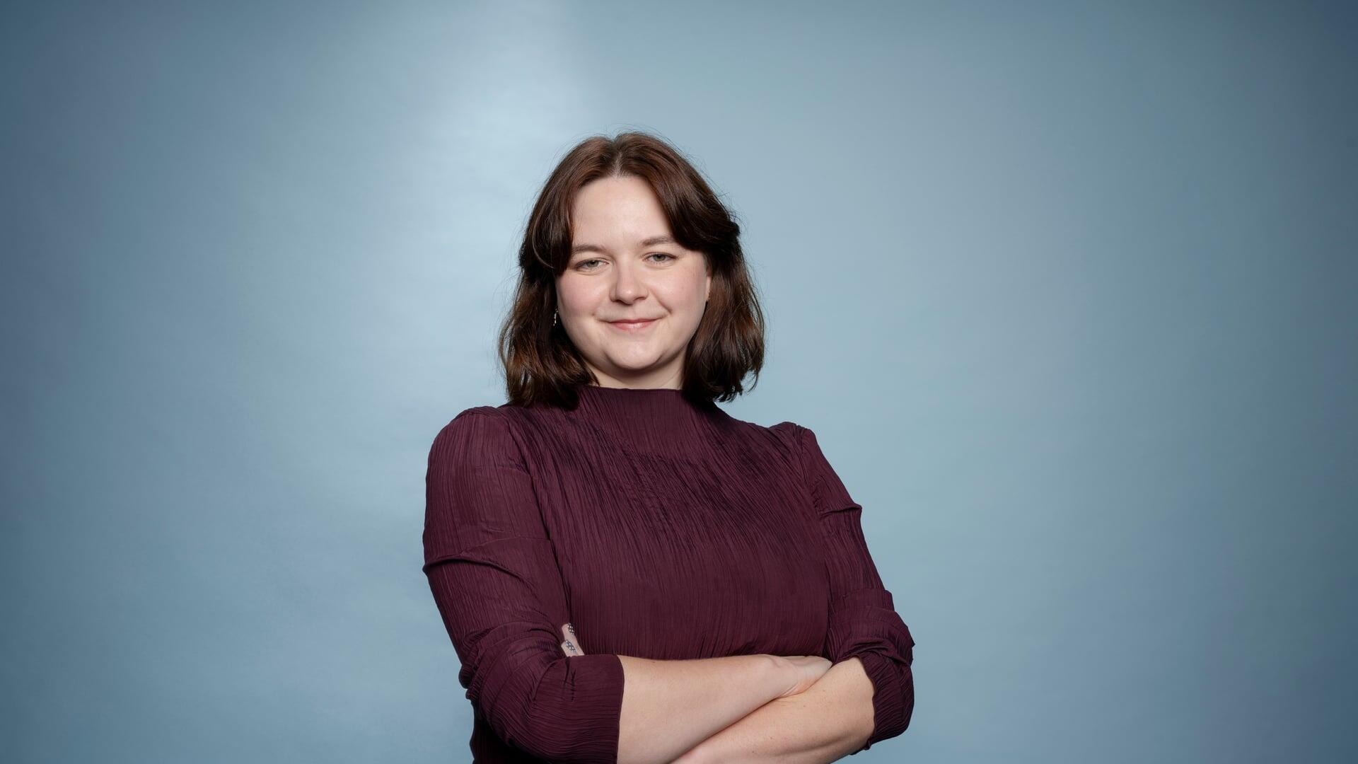 Roos kijkt met haar armen over elkaar glimlachend de camera in