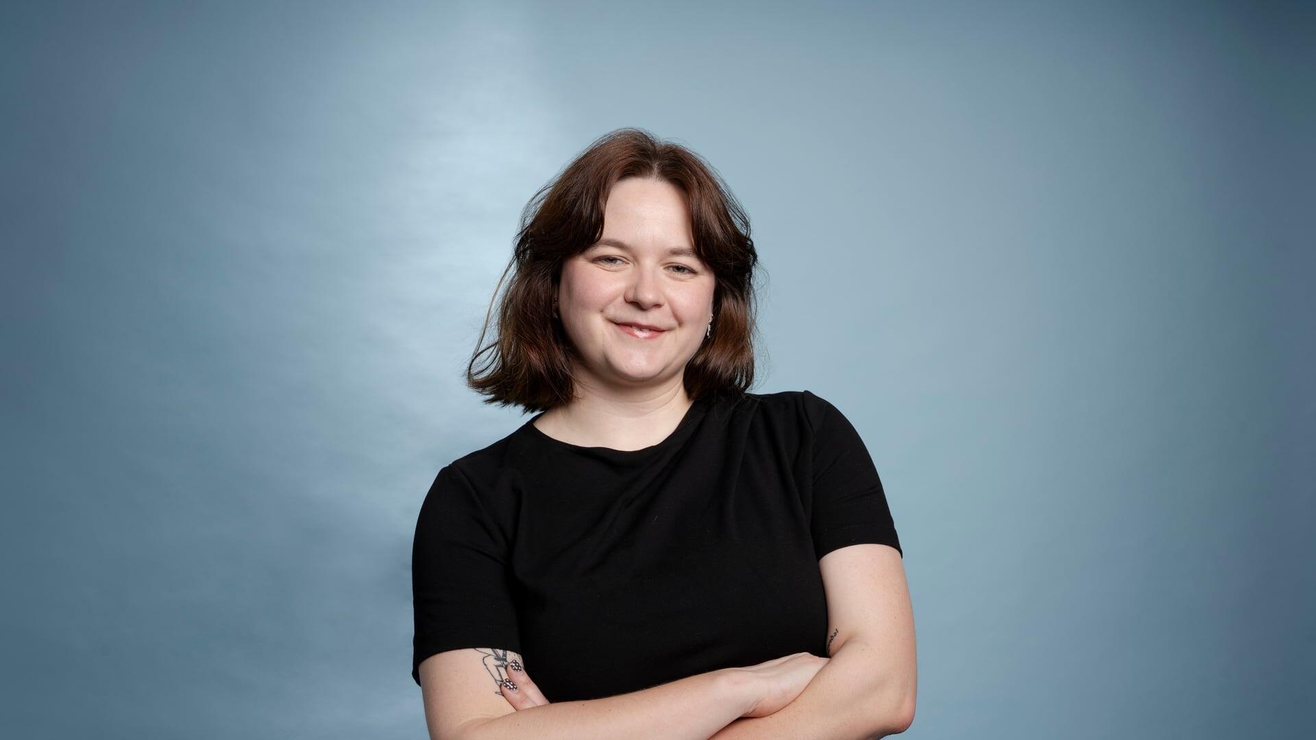 Roos kijkt met haar armen over elkaar glimlachend de camera in