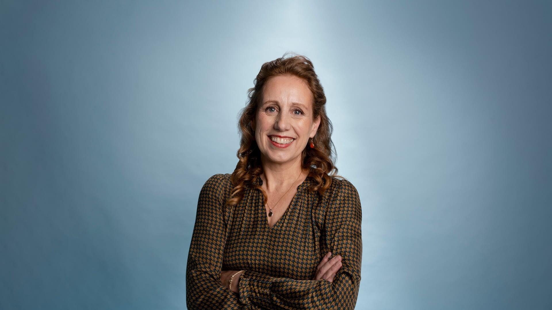 Anneke kijkt met haar armen over elkaar lachend in de camera