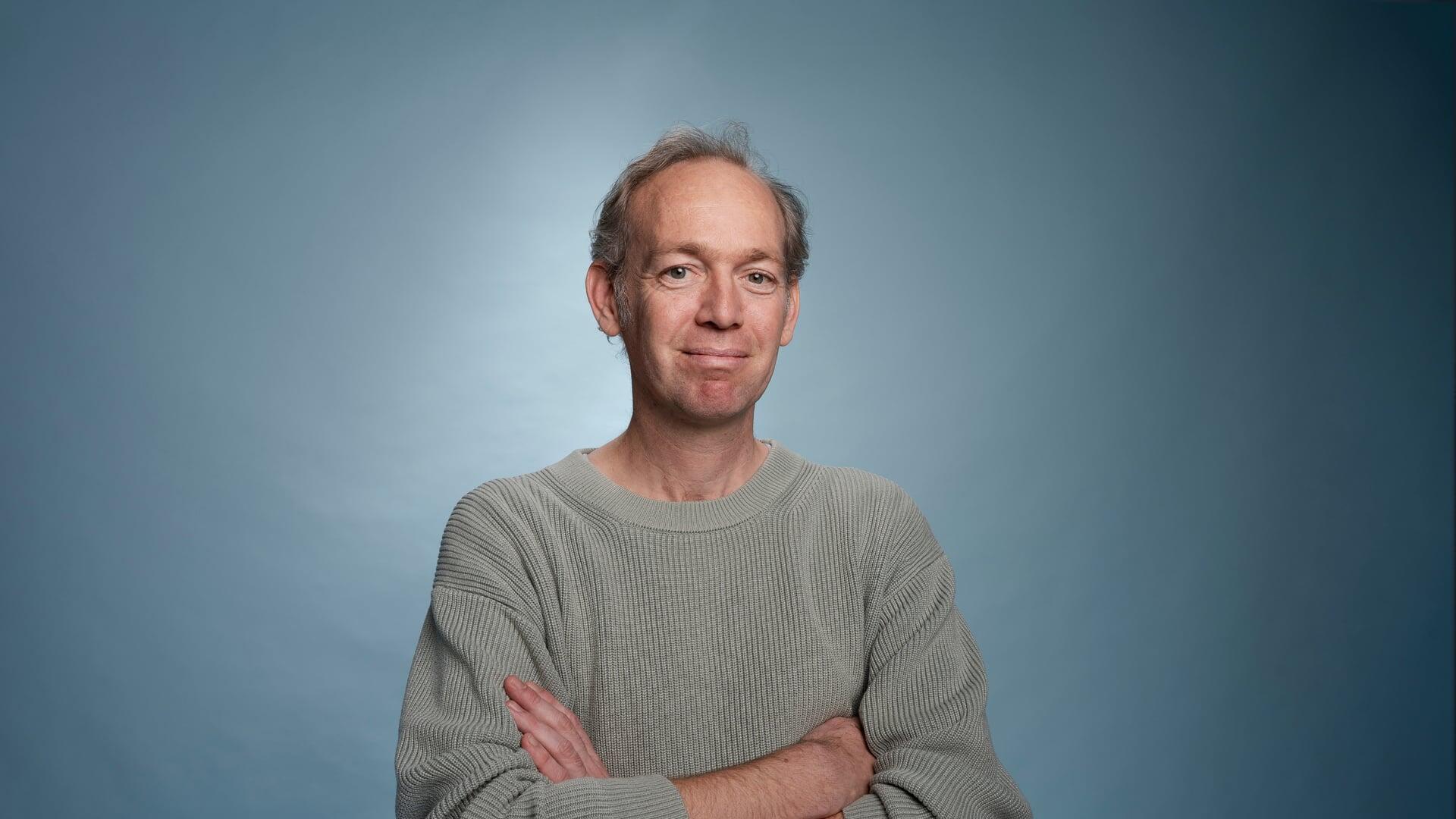 Wijbe kijkt met zijn armen over elkaar glimlachend de camera in