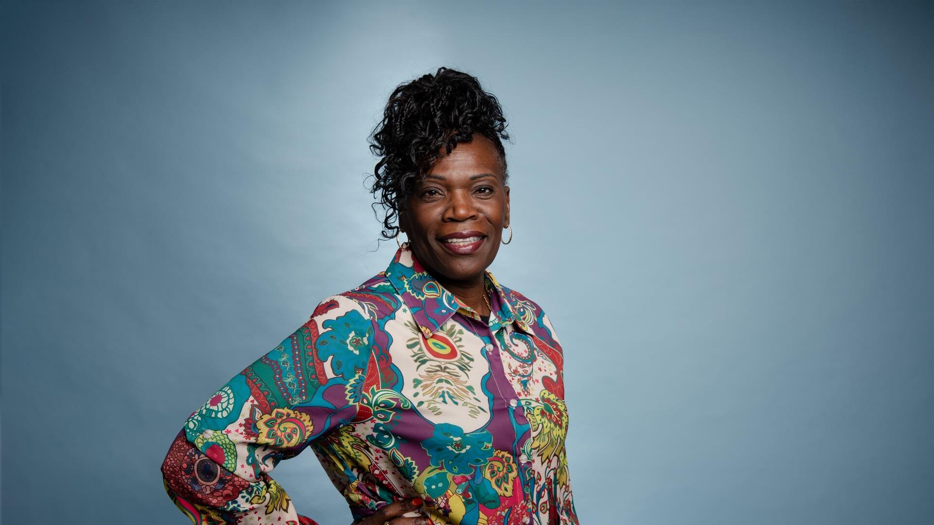 Imelda kijkt met haar hand in haar zij lachend de camera in