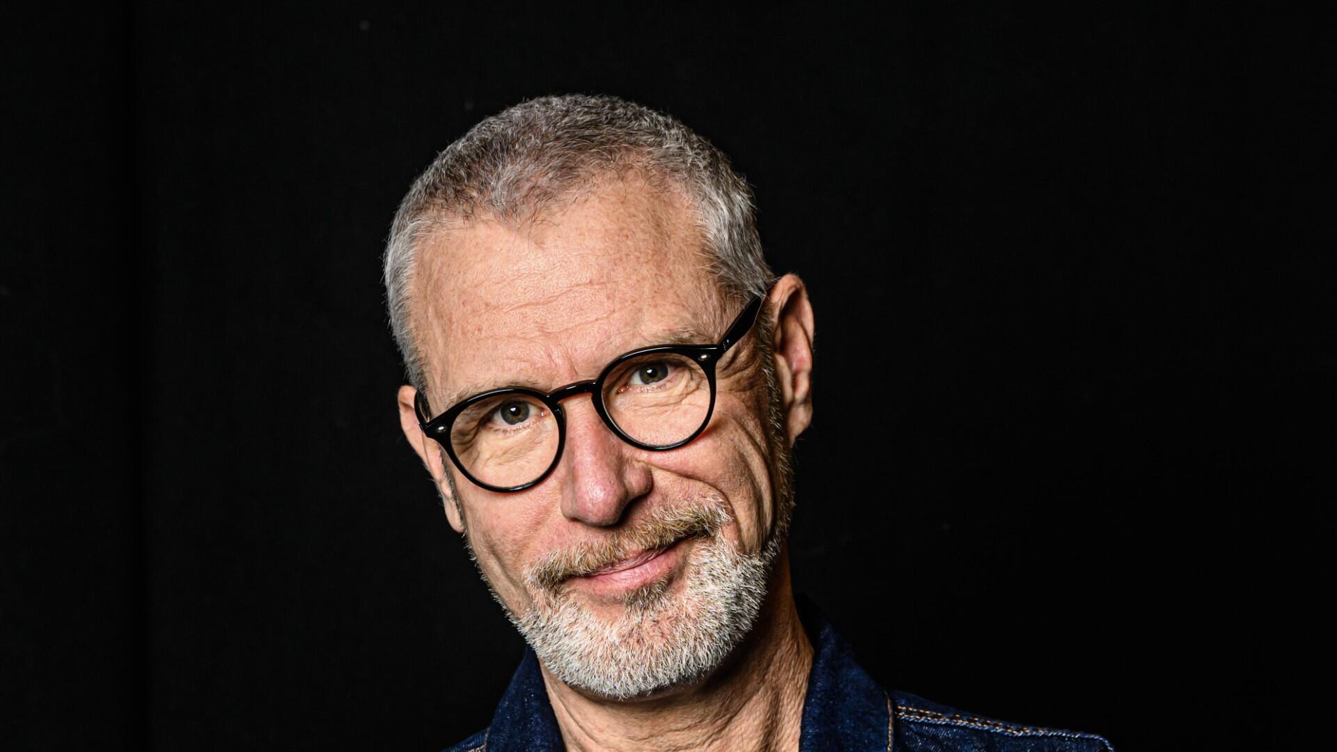 Eric kijkt met zijn armen over elkaar lachend de camera in