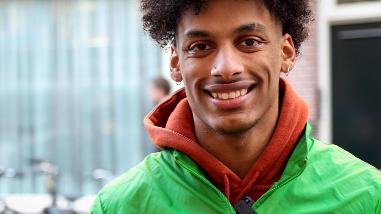 Ibrahim op pad in West met een GroenLinks jas aan, terwijl hij lachend de camera in kijkt
